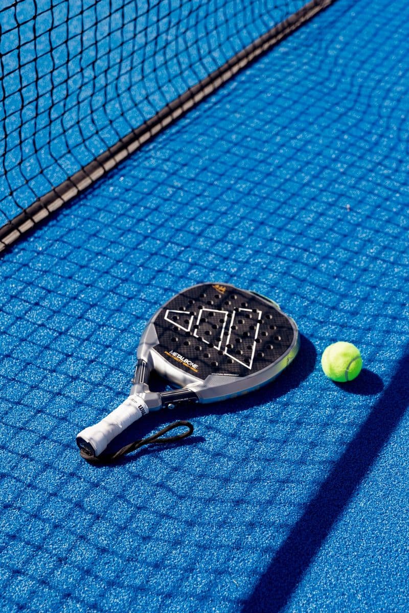 Padel-Schläger und Ball am Netz auf blauem Court